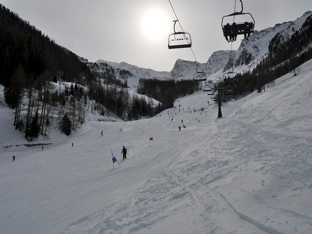 Sessellift über der Piste, die Sonne steht tief über dem Grat.